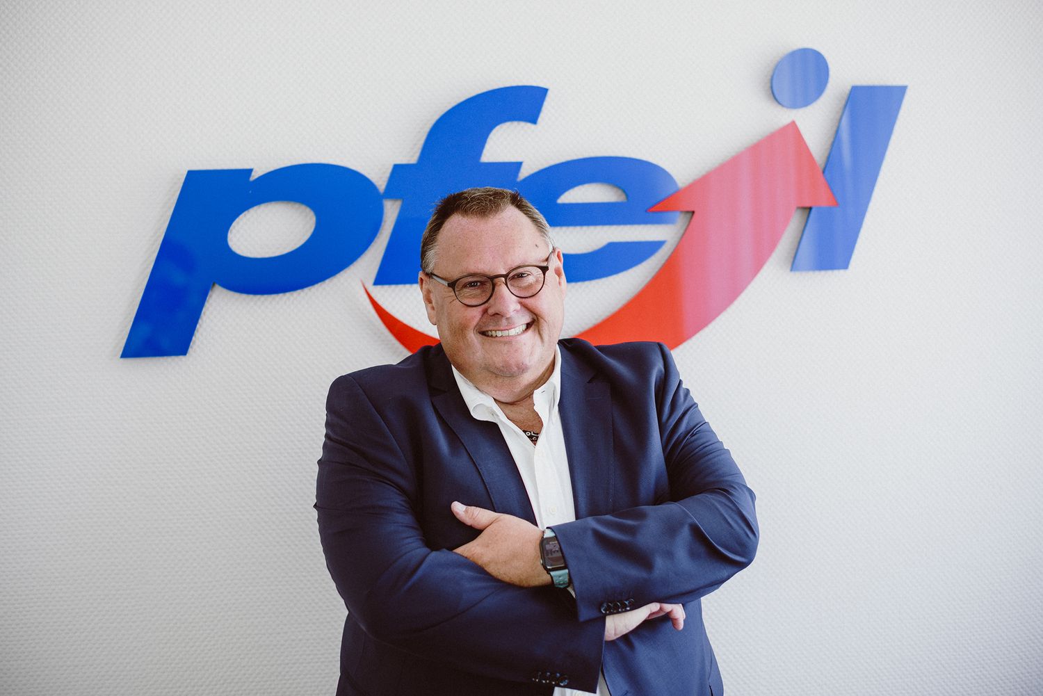 Business professional posing in front of blue company logo on white wall.