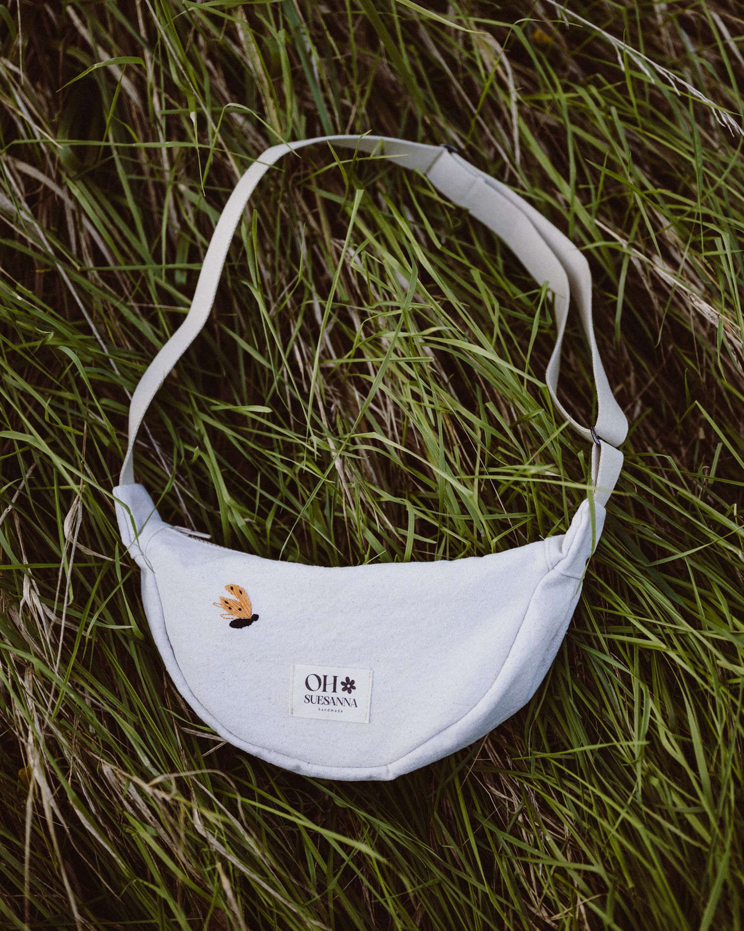 White fanny pack with embroidered design lying on tall grass.
