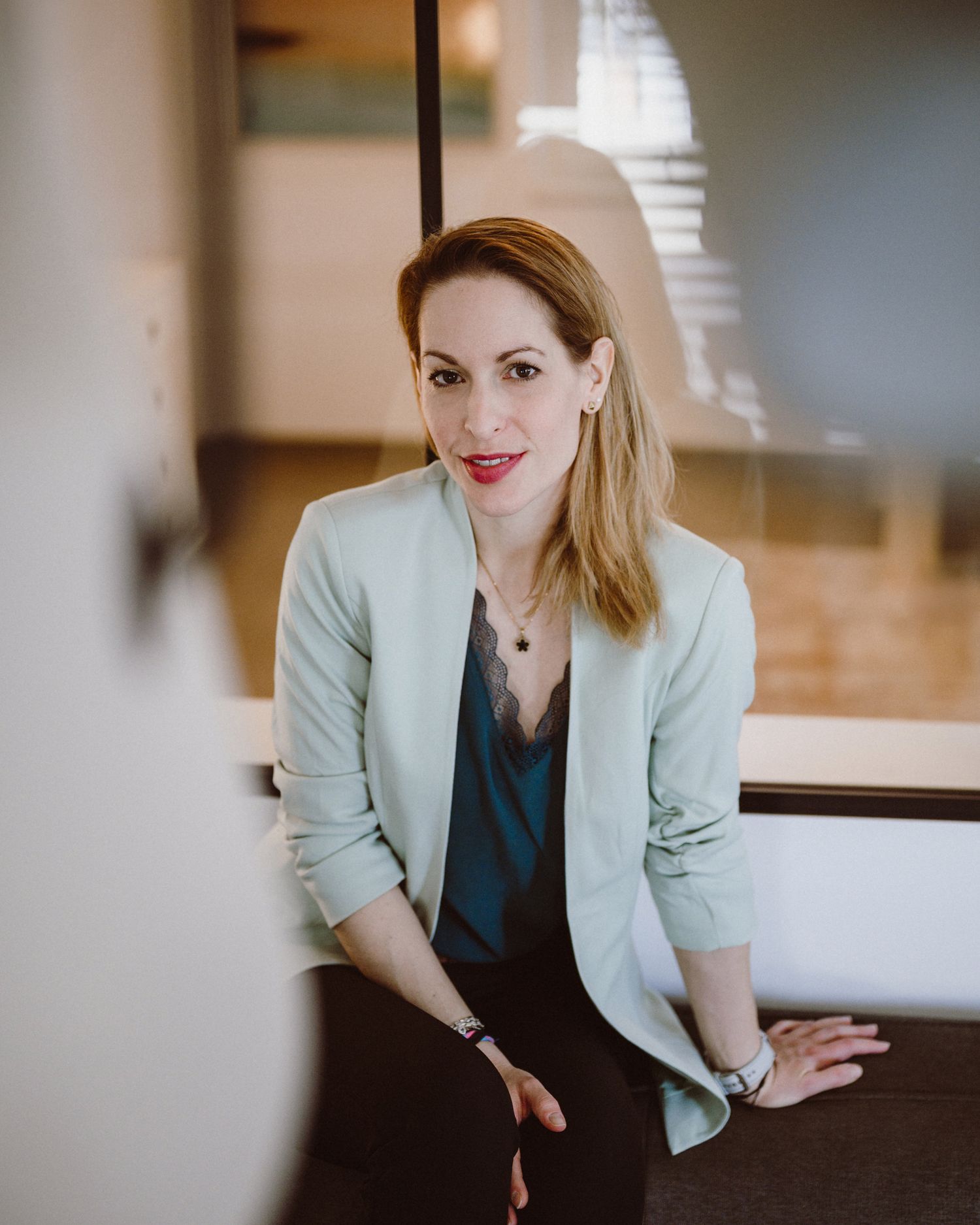 Professional headshot of someone in a mint blazer and dark blouse against an interior office background.