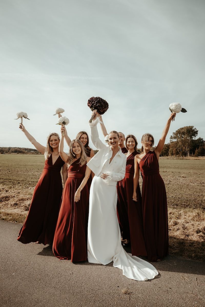 Gruppbild på elegant brud iklädd vitt och hennes brudtärnor iklädda bordeauxfärgade klänningar. Foto av Grevholm Photography