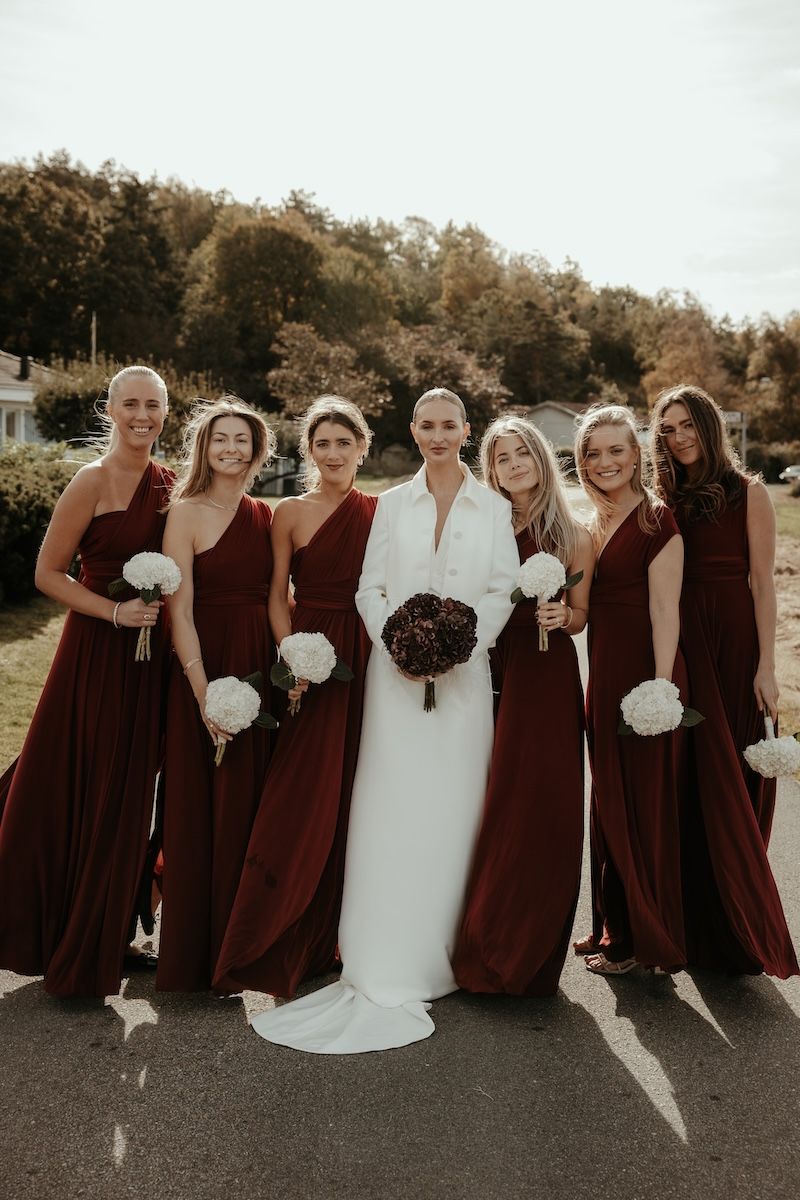 Gruppbild på elegant brud iklädd vitt och hennes brudtärnor iklädda bordeauxfärgade klänningar. Foto av Grevholm Photography