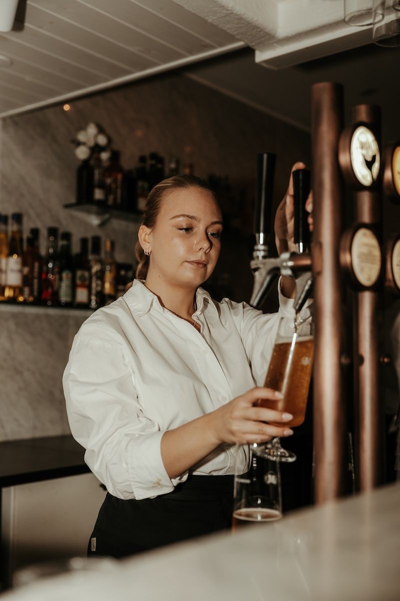 En kvinnlig bartender tappar upp en öl i ett glas under ett bröllop på Särö, fotograferat av Grevholm Photography