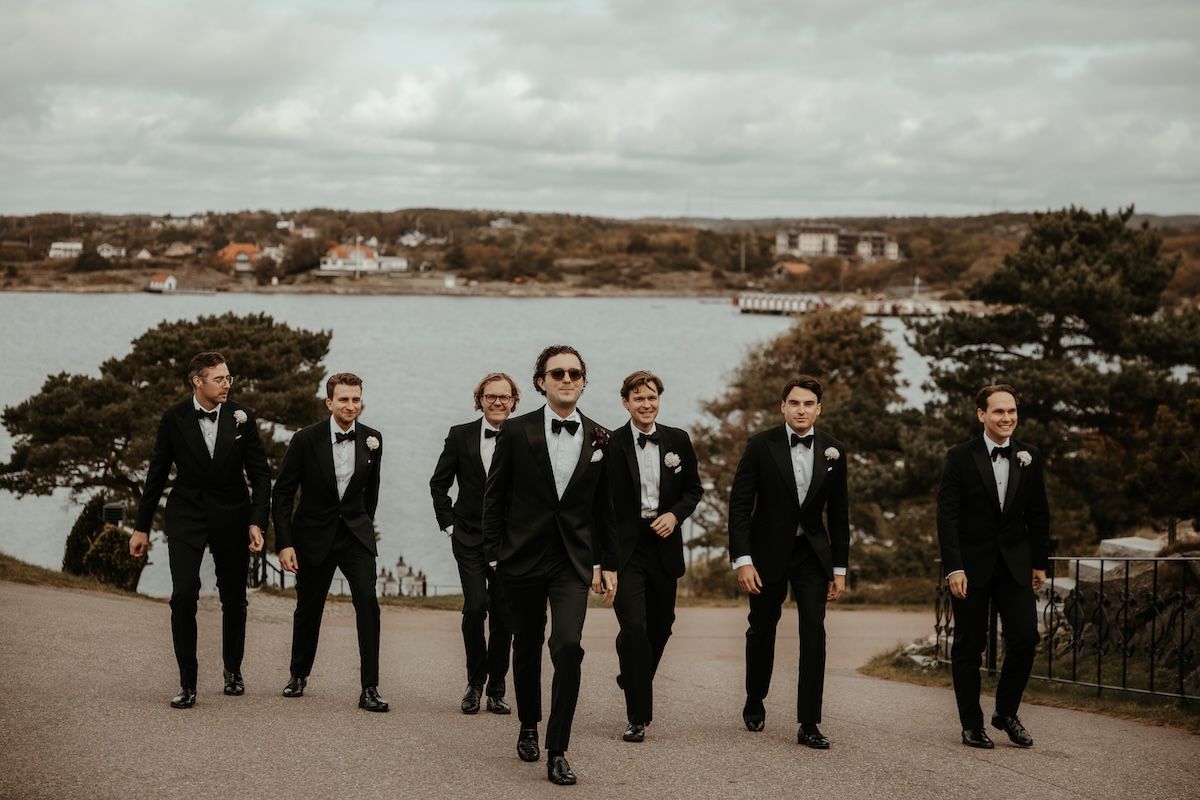 Gruppbild av en brudgum och hans marskalker som går längs en väg. Foto av Grevholm Photography