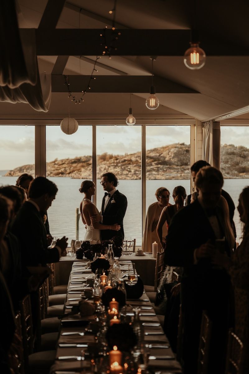 Silhuetter av ett brudpar som står framför ett fönster i festlokalen på deras bröllop. Foto av Grevholm Photography