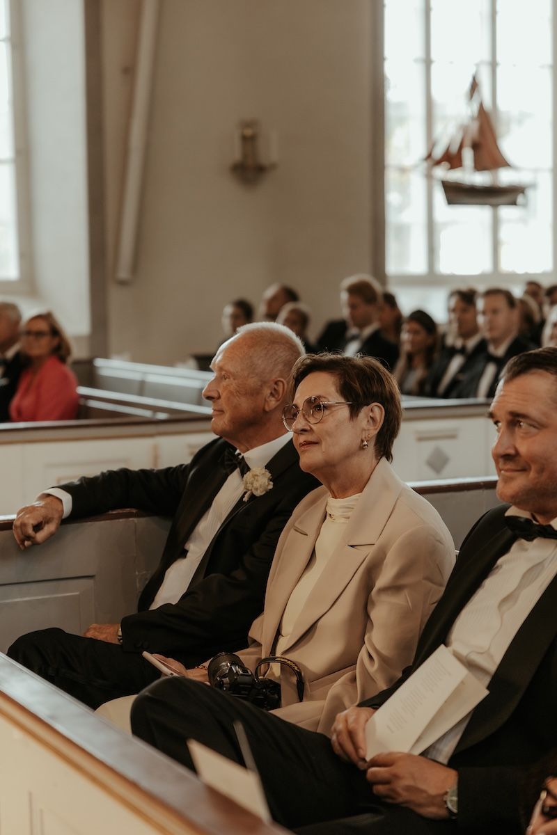 Mamman till bruden ser stolt ut när hon sitter i kyrkbänken av sin dotters bröllop. Foto av Grevholm Photography