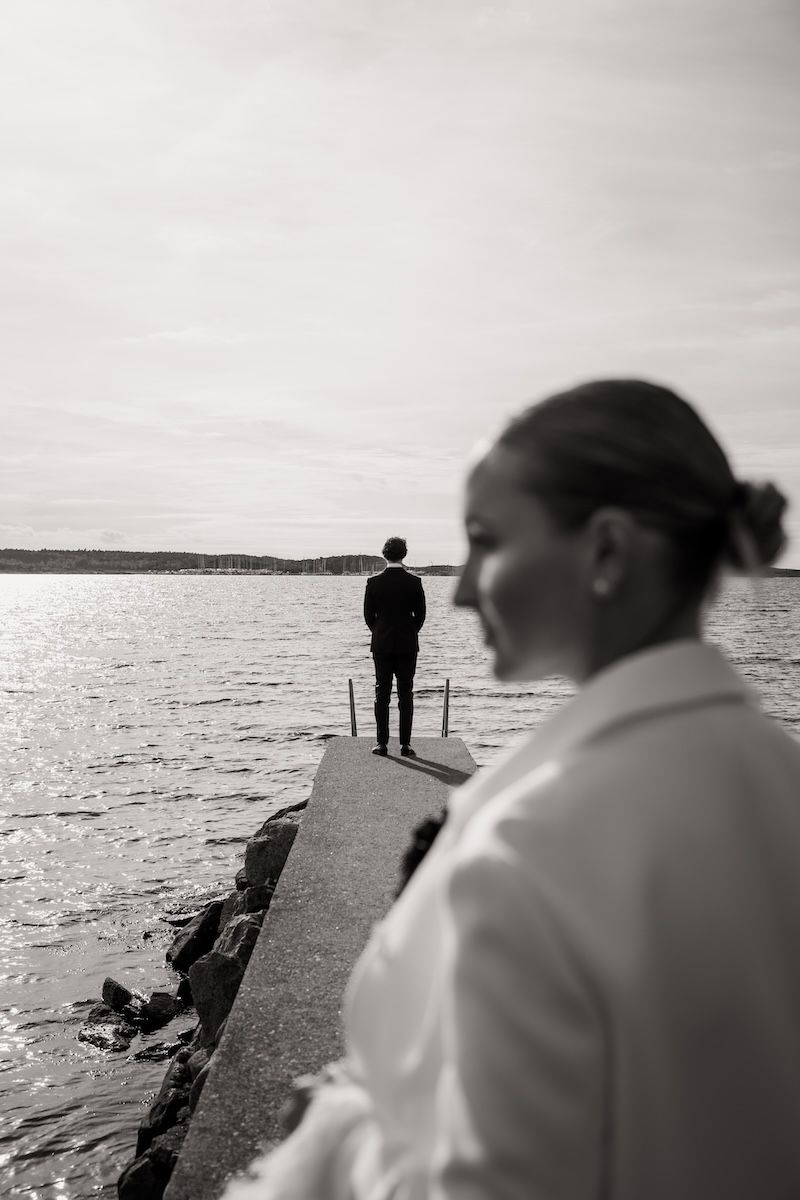 Brudgum står längst ut på en brygga och väntar på sin brud innan en first look på deras bröllopsdag. Foto av Grevholm Photography