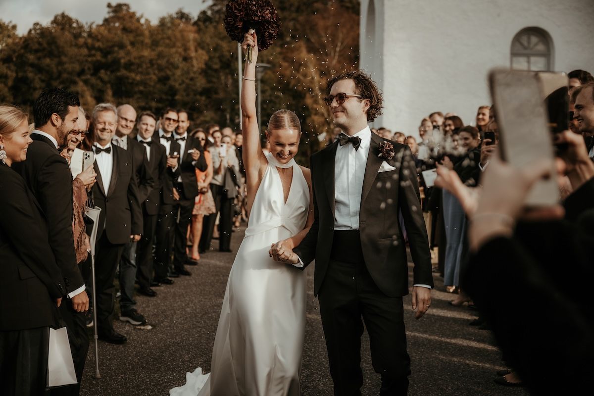Brudpar tar emot jubel och gratulationer av sina gäster som kastar ris på dem när de går ut från kyrkan efter deras vigsel i Släps kyrka.