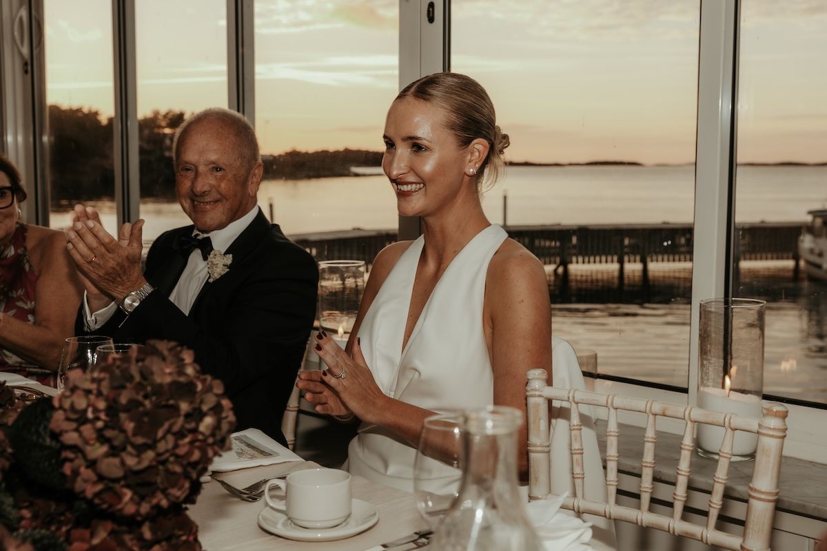 Brud applåderar efter att hennes man hållit ett tal på Blomstermåla Särö, fotograferat av Grevholm Photography.