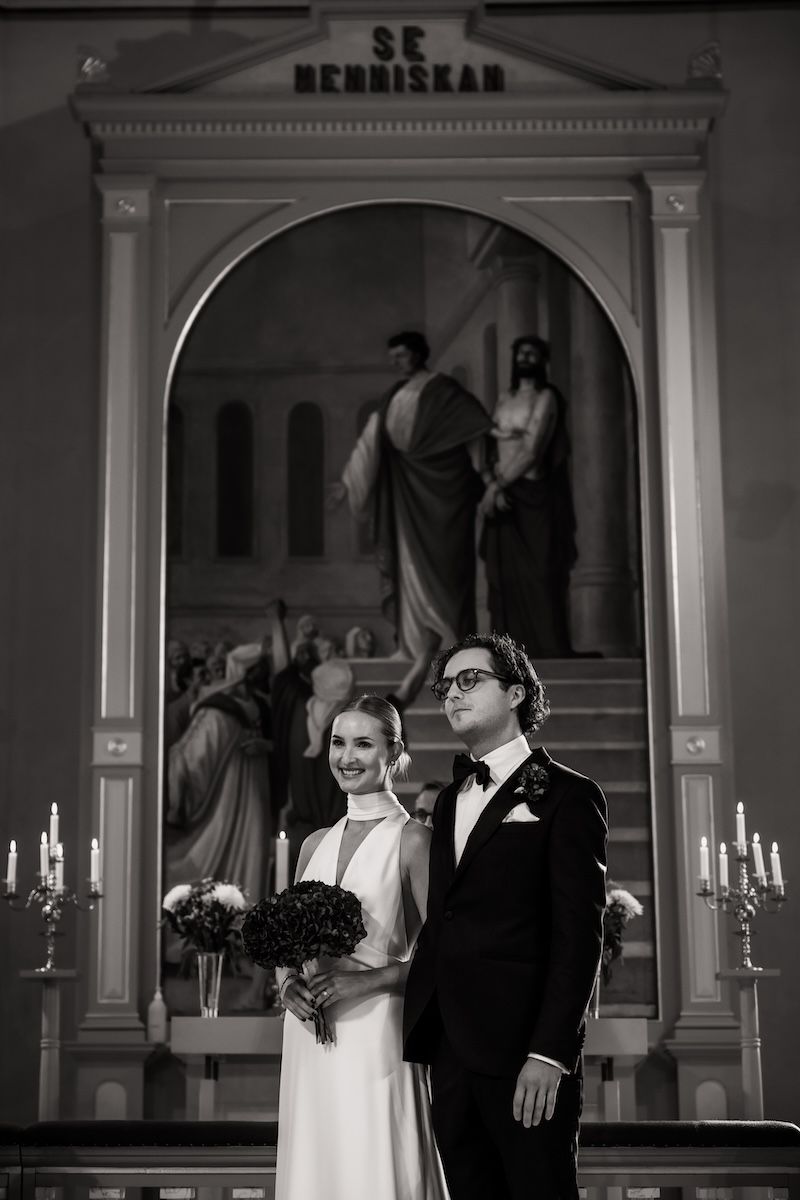 Ett tidlös foto av ett elegant brudpar som står framme vid altaret under deras bröllop i södra Sverige. Foto av Grevholm Photography