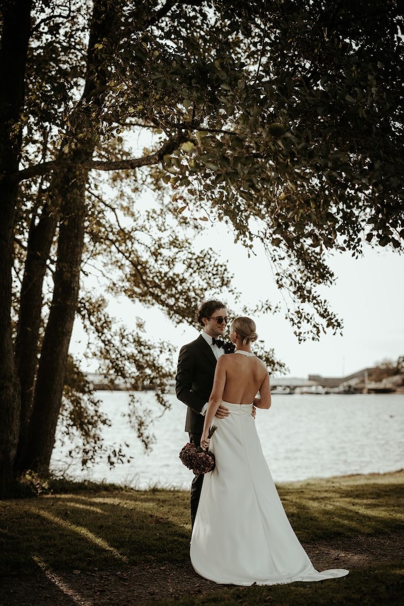 Ett brudpar omfamnar och kysser varandra i grönskande miljö under deras bröllop på Särö. Foto av Grevholm Photography