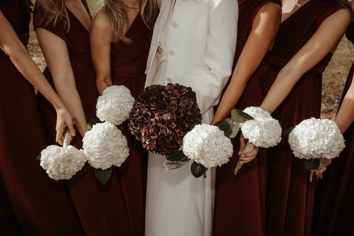 Gruppbild på elegant brud iklädd vitt och hennes brudtärnor iklädda bordeauxfärgade klänningar. Foto av Grevholm Photography