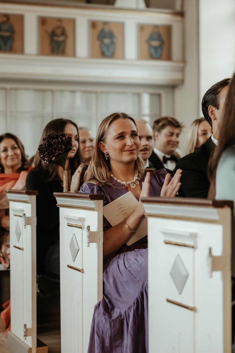 En bröllopsgäst applåderar efter solosång under ett bröllop i en kyrka. Foto av Grevholm Photography