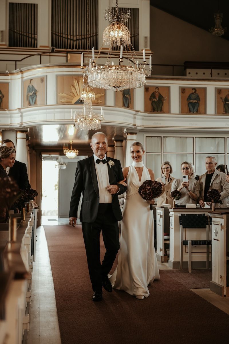 Bruden och hennes pappa går ner för altaret i en vacker kyrka. Foto av Grevholm Photography