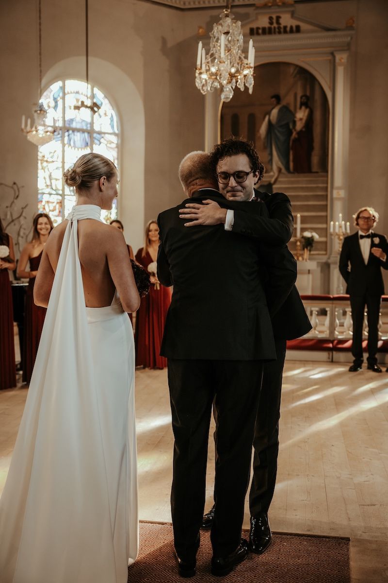 Pappan till bruden kramar om brudgummen när han överlämnar bruden till honom vid altaret. Foto av Grevholm Photography