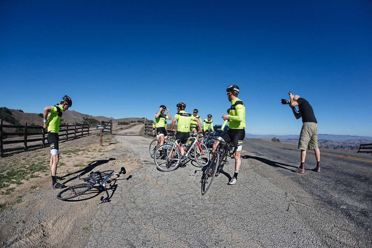 Group of cyclists in high-visibility gear gathered on mountain road for photo opportunity.