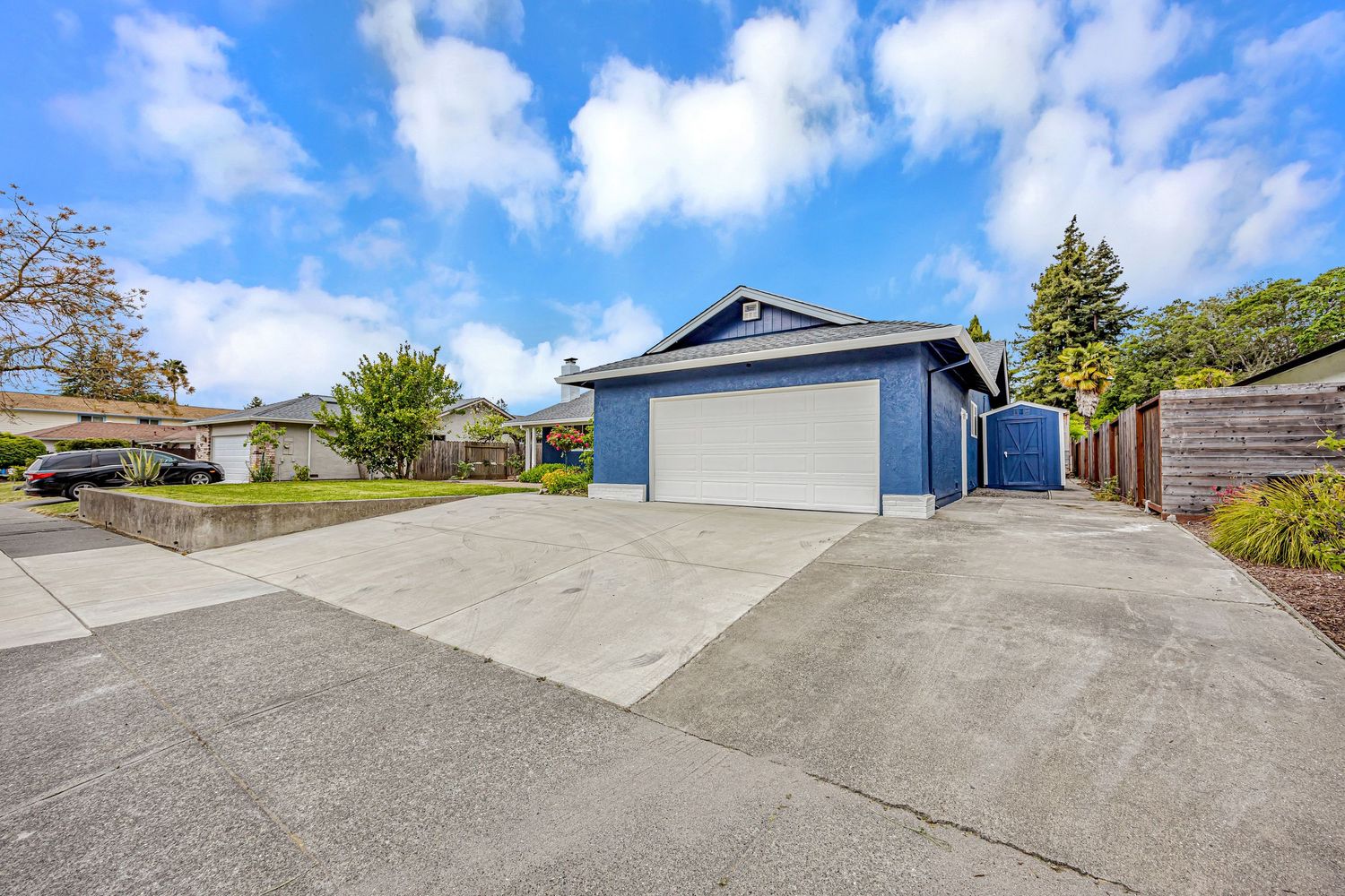 Blue garage with concrete driveway under bright blue sky with white puffy clouds.