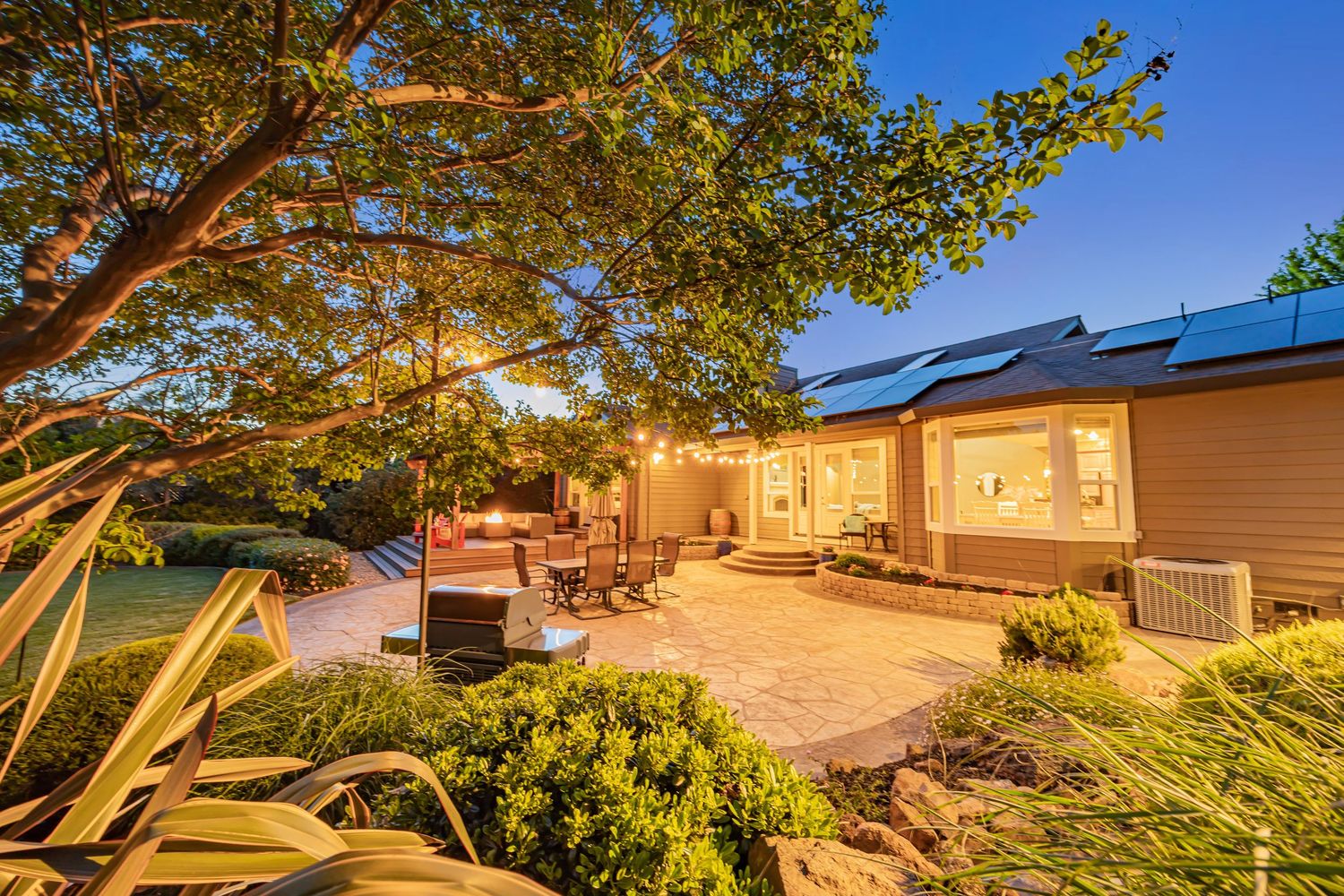 Backyard patio space with string lights and mature trees creating a cozy evening atmosphere.