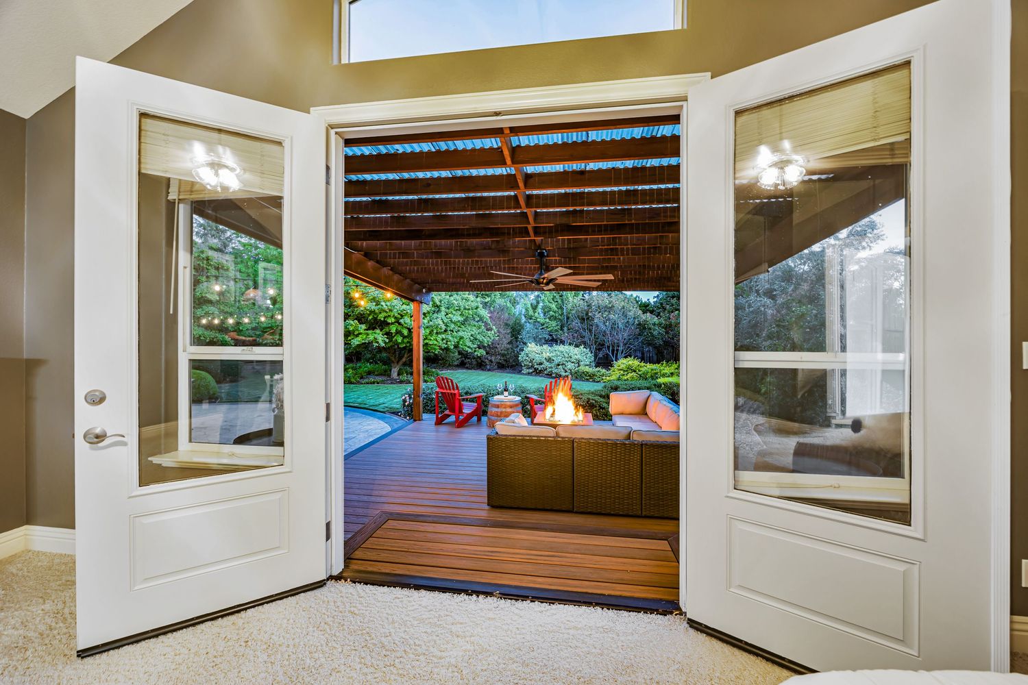 French doors open to spacious deck with red outdoor furniture and pergola covering.