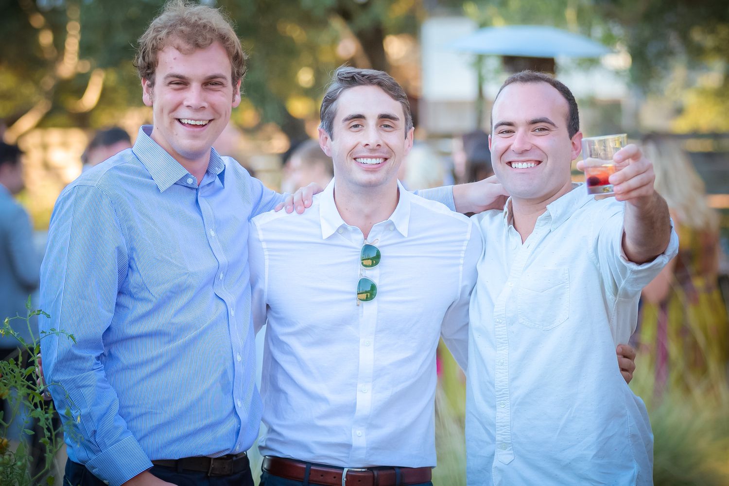 Three friends in casual attire smiling outdoors at sunset.