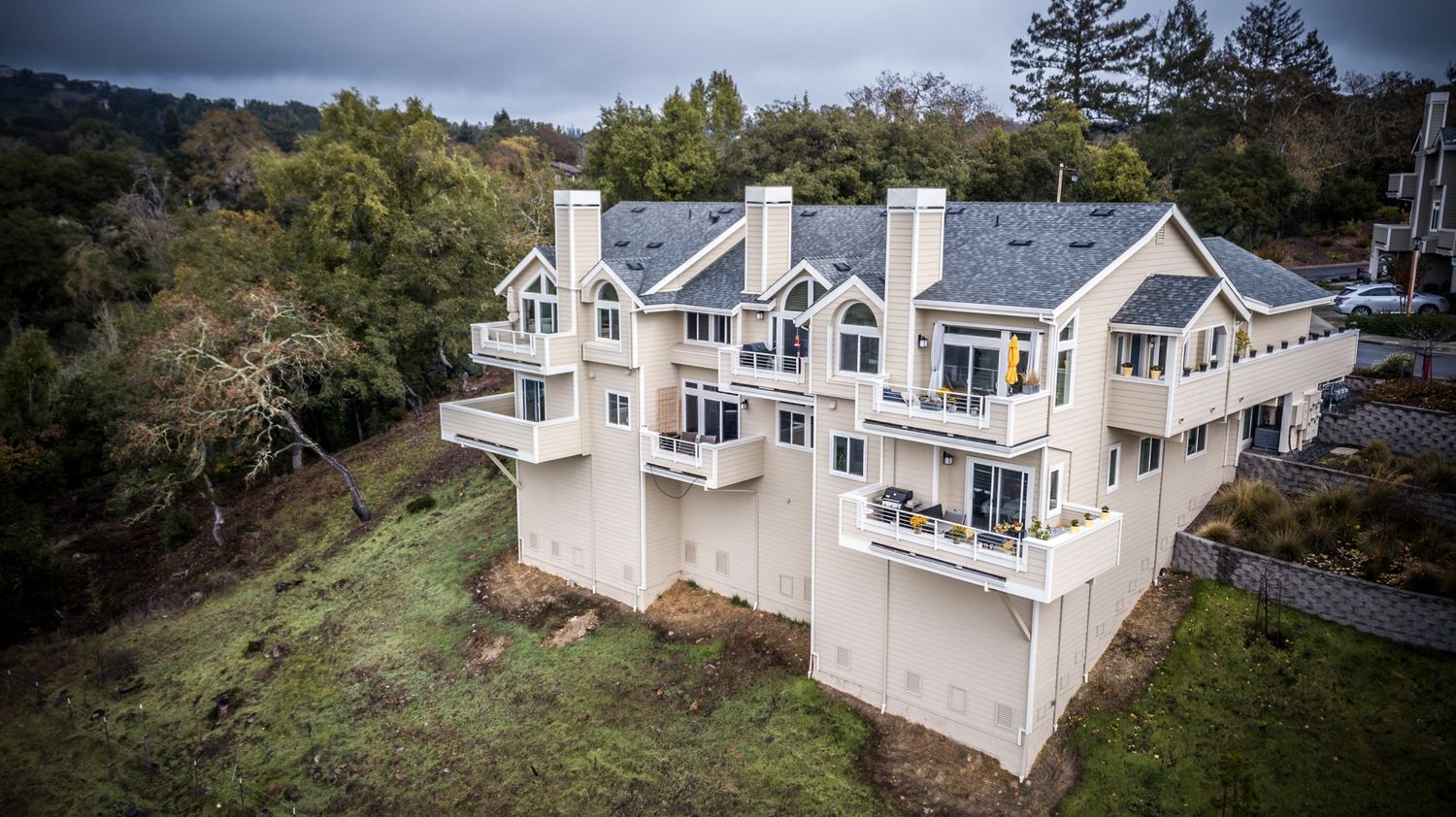 Large contemporary white multi-level home with balconies built into hillside under cloudy skies.