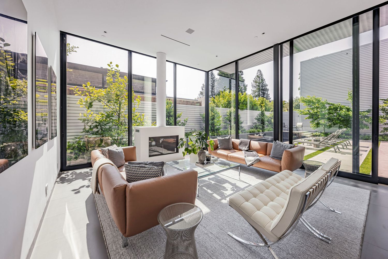 Luxurious living room with tan leather seating, glass walls, and outdoor views surrounded by greenery.