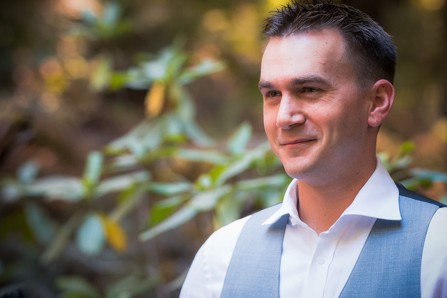Candid portrait of groom in grey vest smiling outdoors.