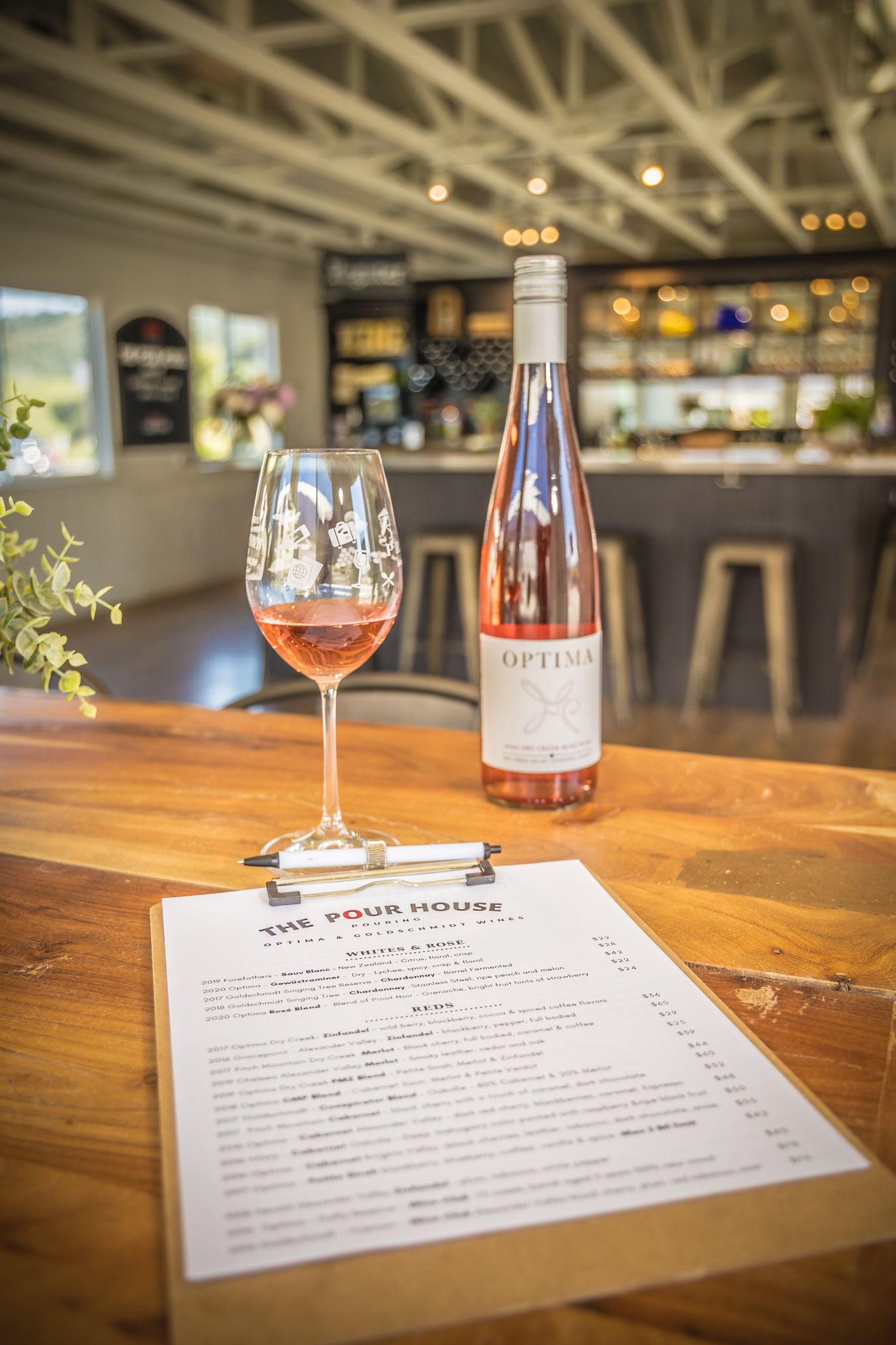 A glass of rosé wine and menu on a wooden table in a restaurant with blurred background lighting.
