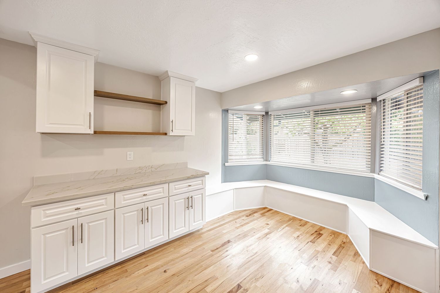 Modern kitchen remodel with white cabinets, bay window seating area, and hardwood flooring.