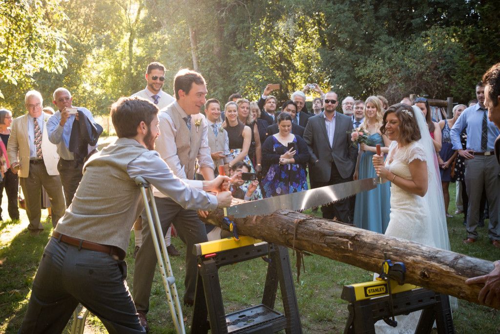 Wedding guests sawing a log together during an outdoor reception activity.