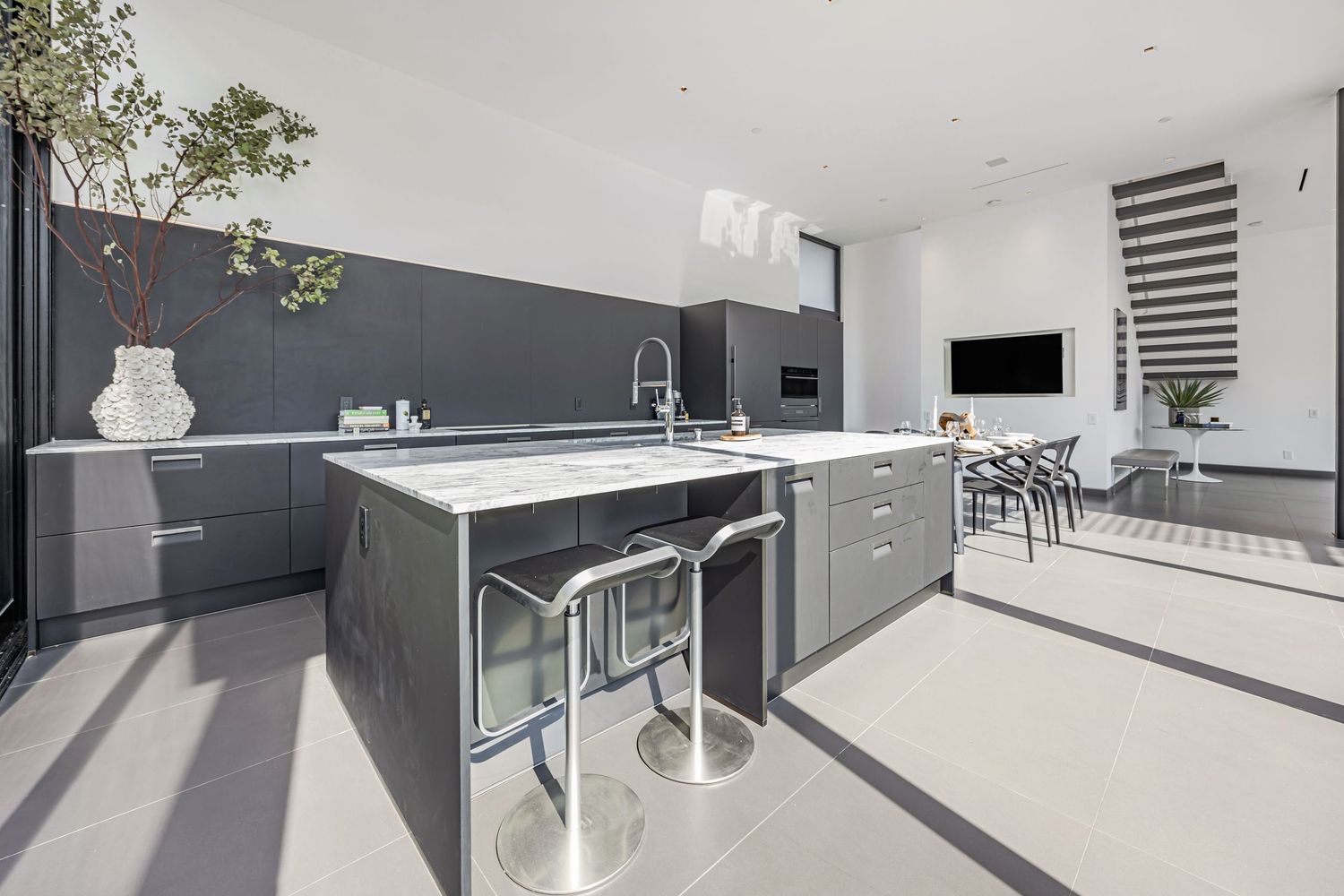 Contemporary open-plan kitchen space with grey cabinets and large windows bringing in natural light.