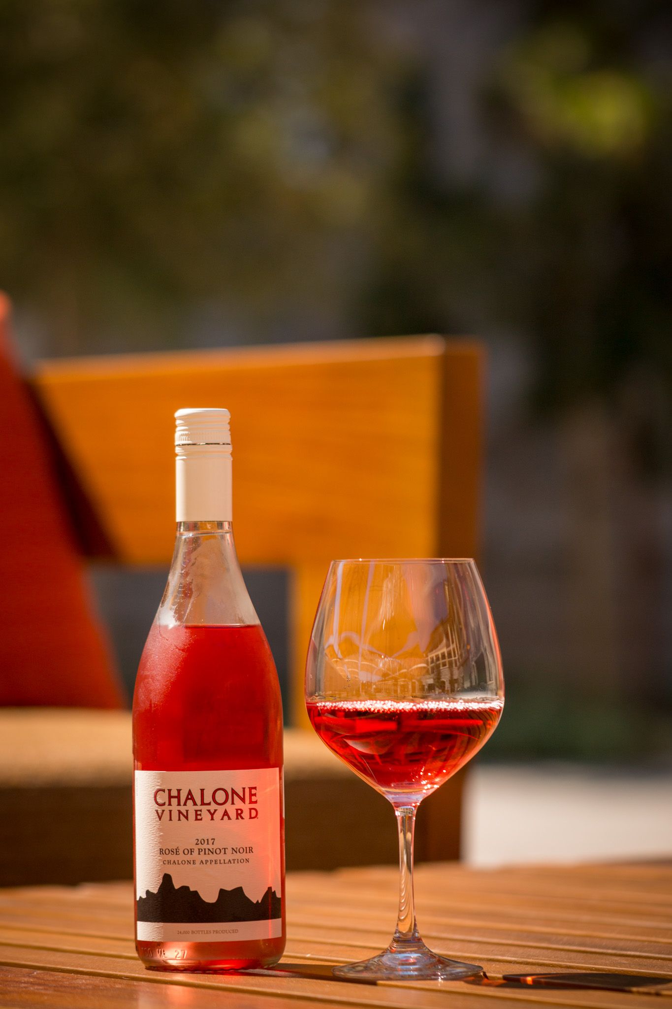 Chalone Vineyards rosé wine bottle and glass on outdoor table with sunset lighting.