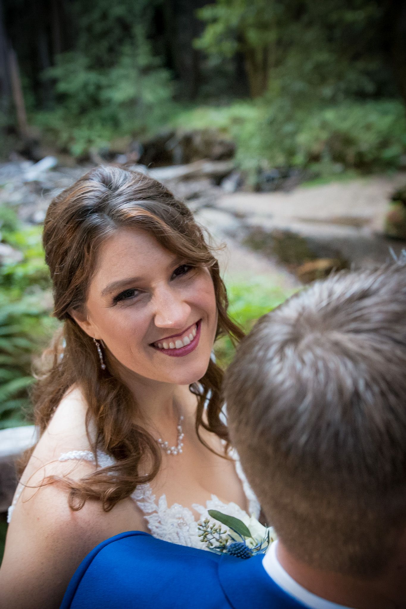 A joyful wedding moment captured in a natural forest setting with delicate bridal jewelry visible.