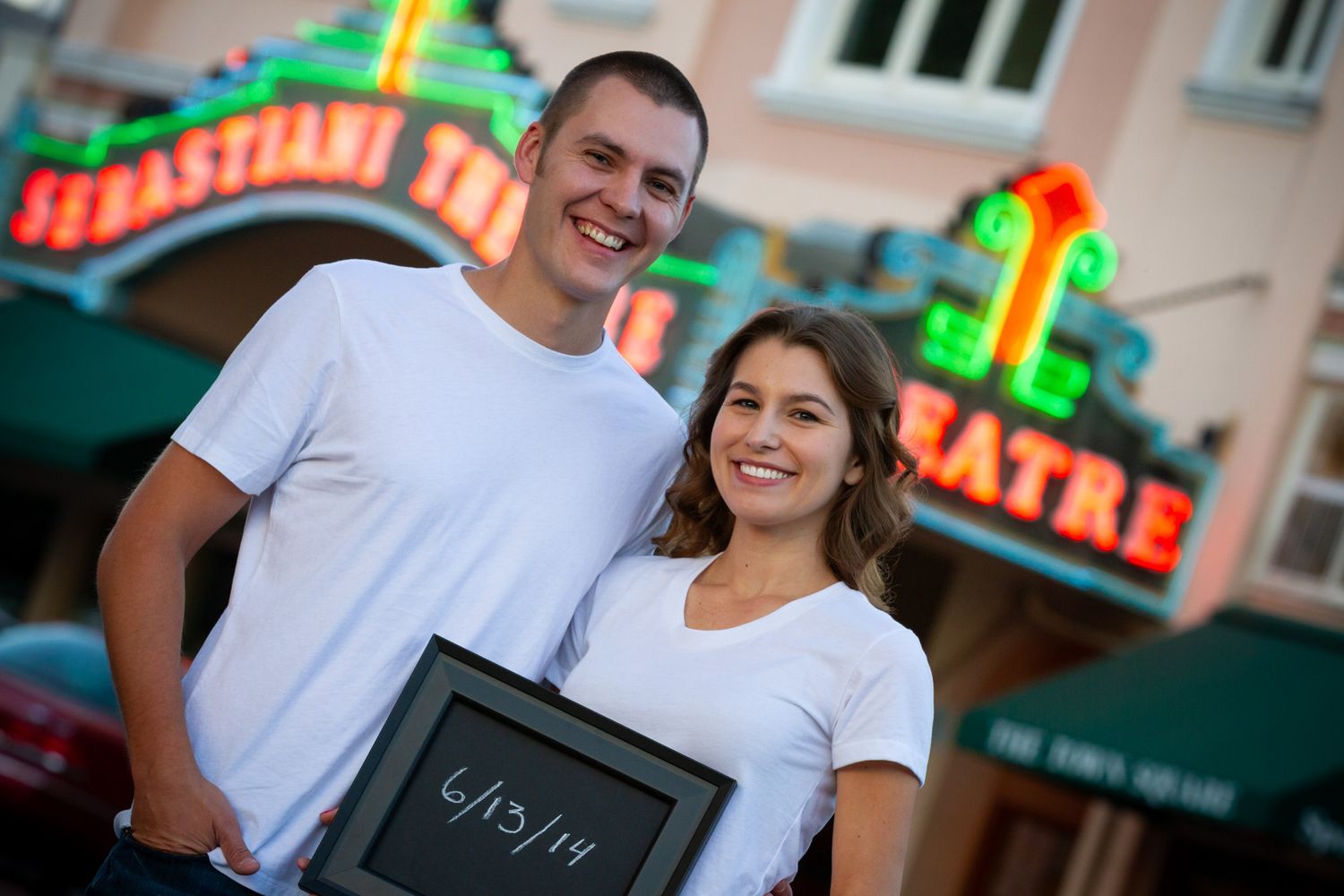 Couple standing outside a pink building with neon signage.