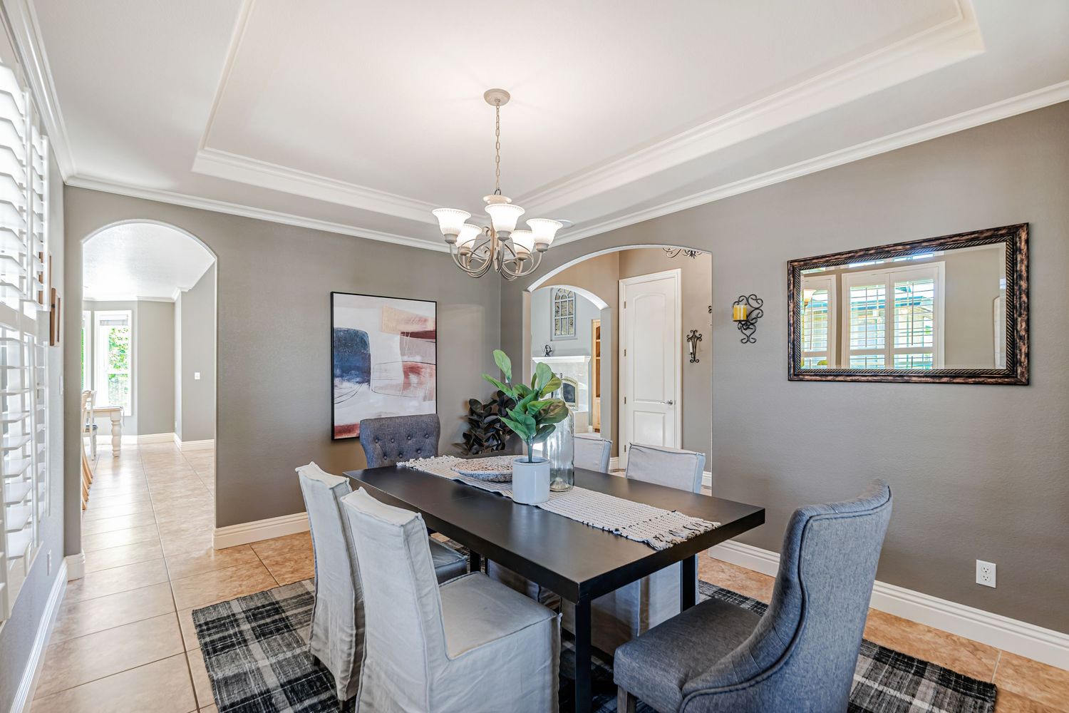 Modern dining area with crystal chandelier, dark wood table, and gray upholstered chairs on plaid area rug.