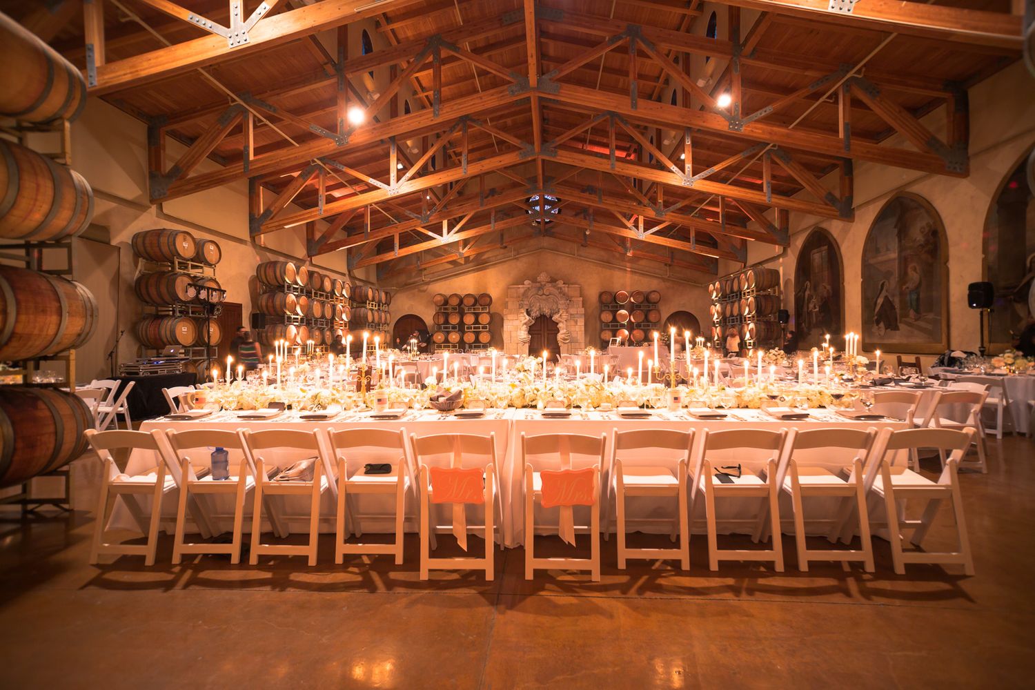 Wedding reception tables set for dinner in a rustic barrel room with warm lighting and exposed wooden beams.