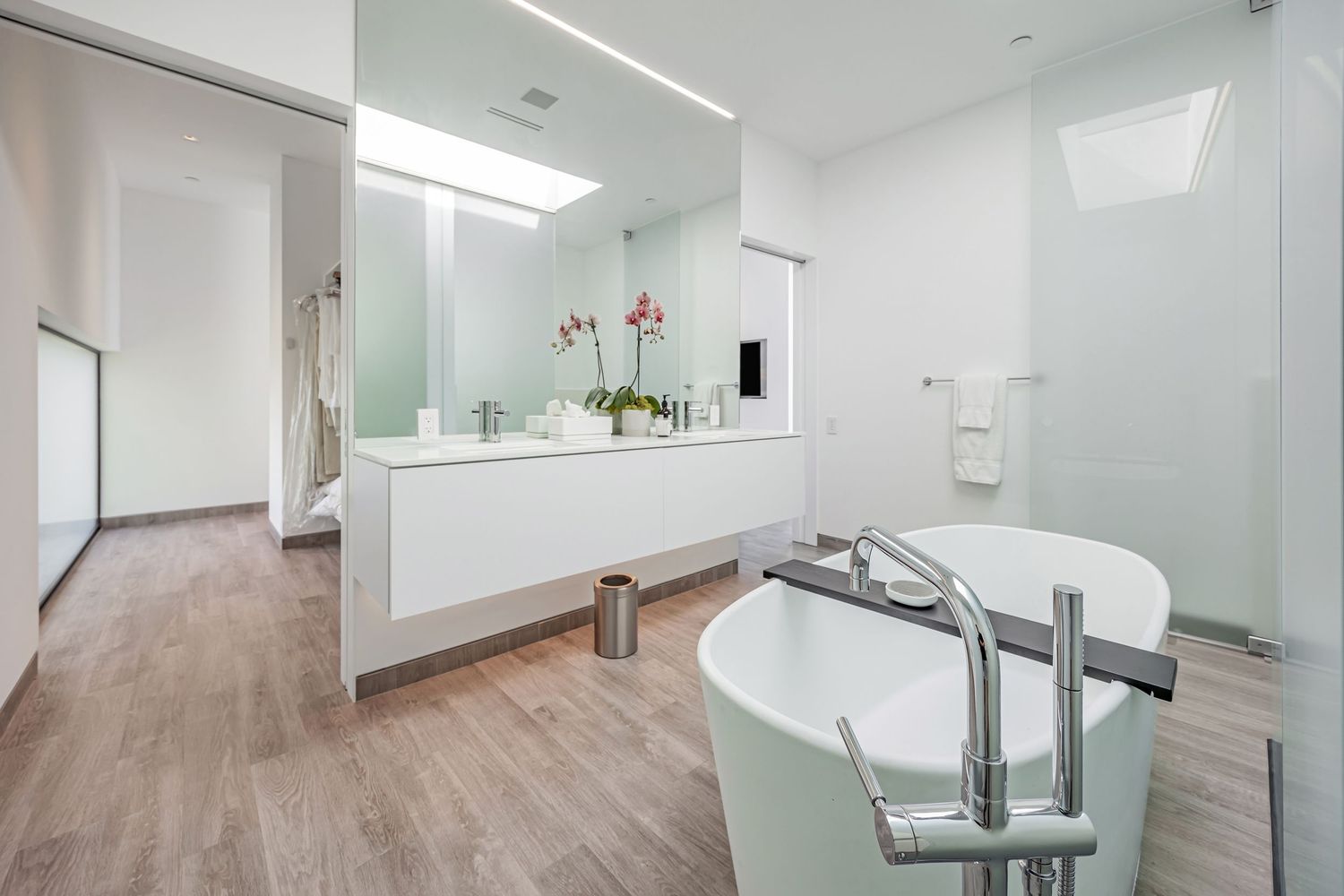 Elegant bathroom featuring a soaking tub and floating vanity with wood flooring.