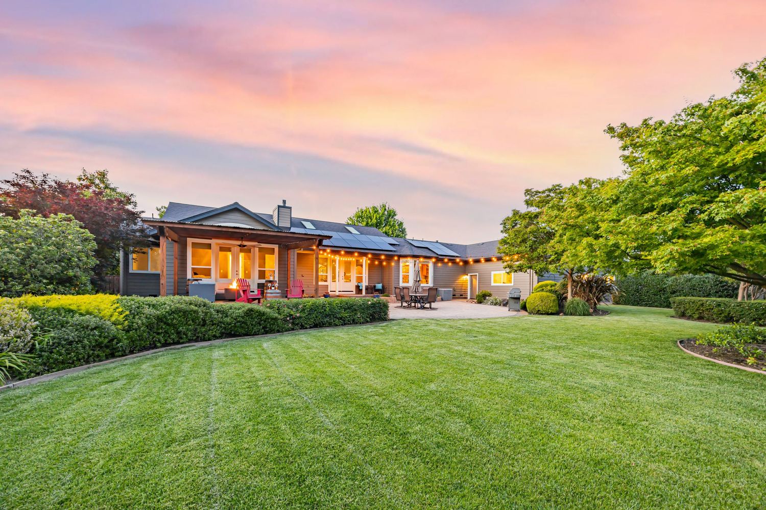Sprawling ranch-style home with manicured lawn glows warmly against pink twilight sky.
