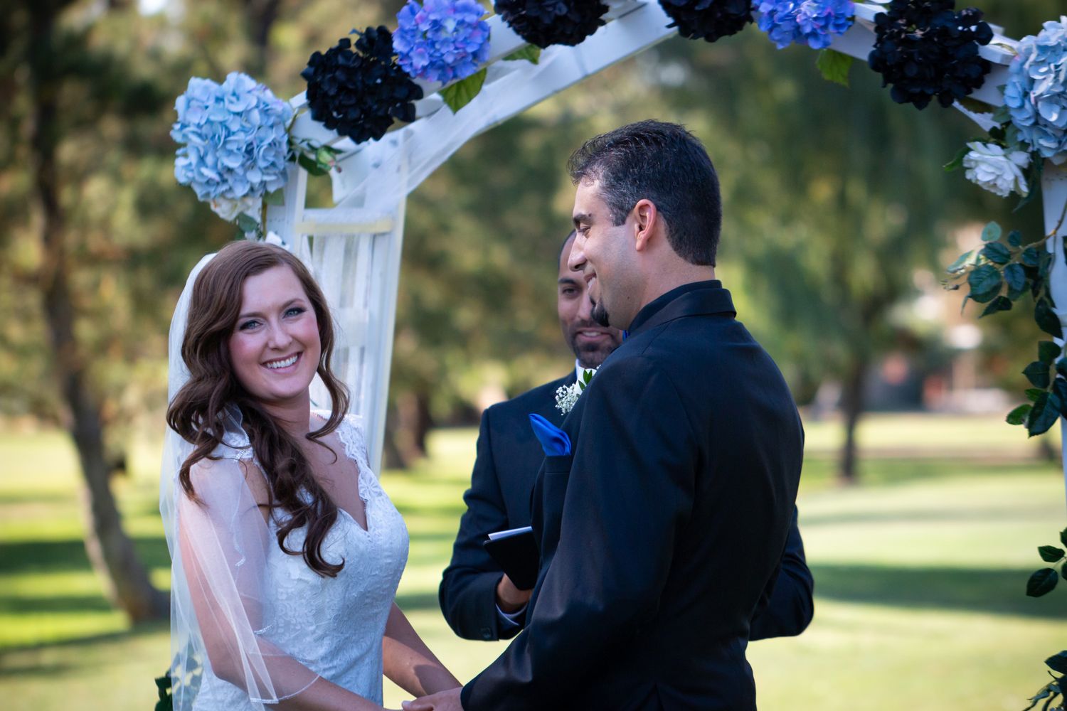 Couple exchanges vows under floral arch with blue hydrangeas.