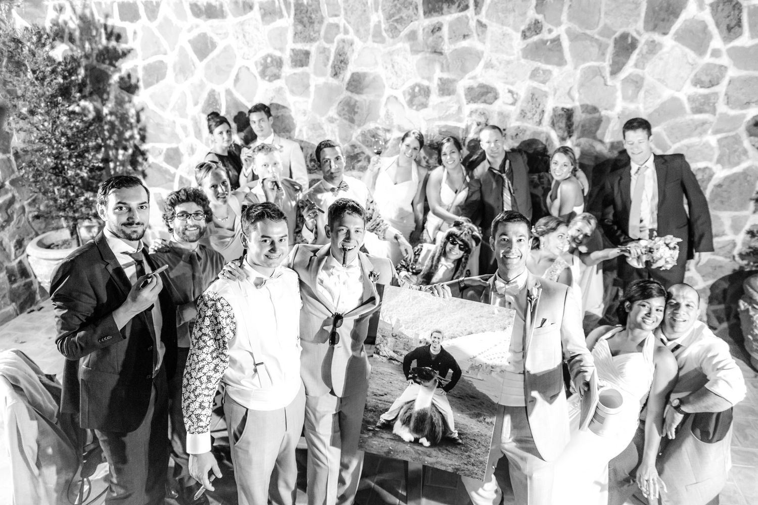 Vintage black and white photograph of a large group gathered together against a stone wall on a sunny day.