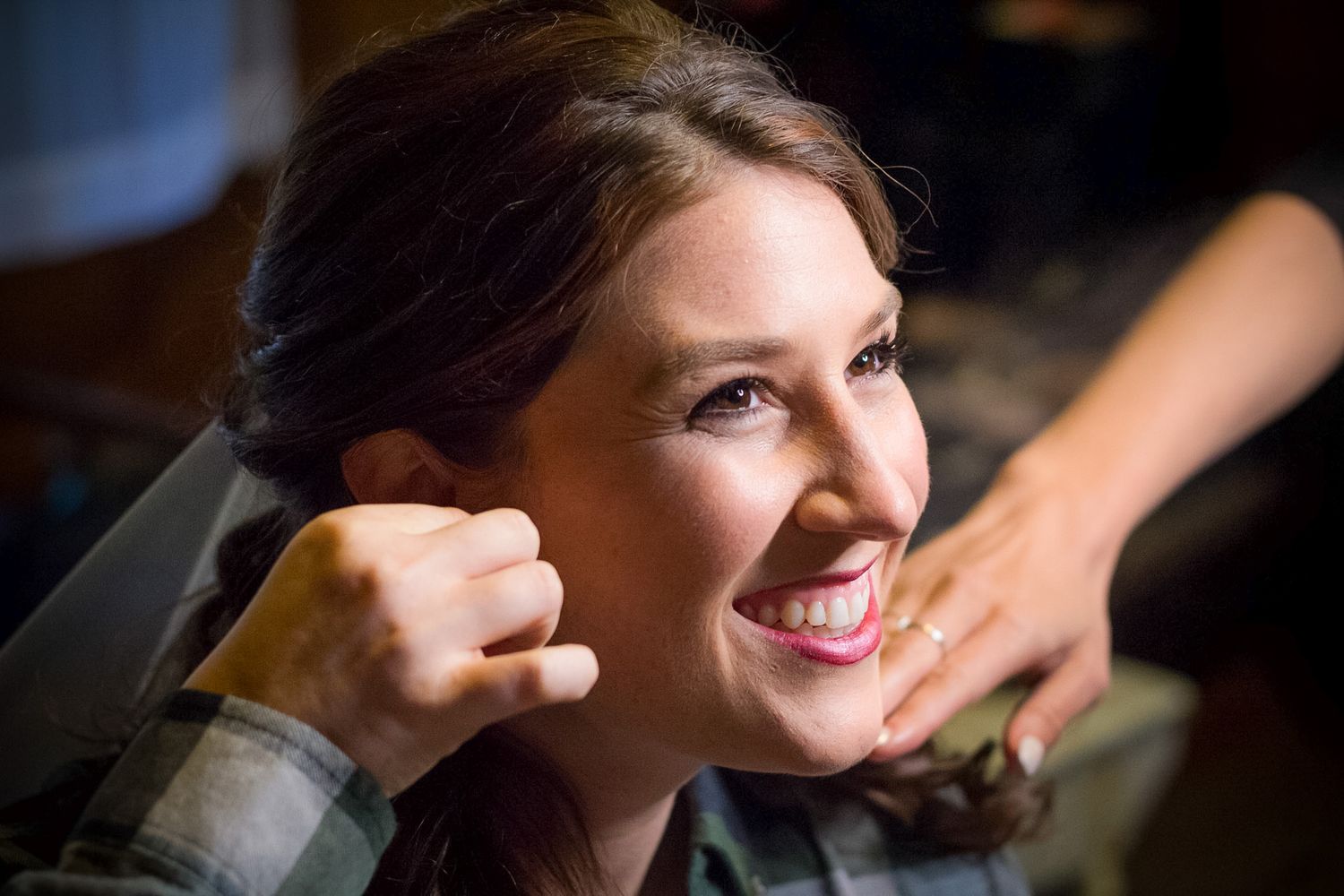 A person getting ready with a joyful expression while someone helps with hair styling.