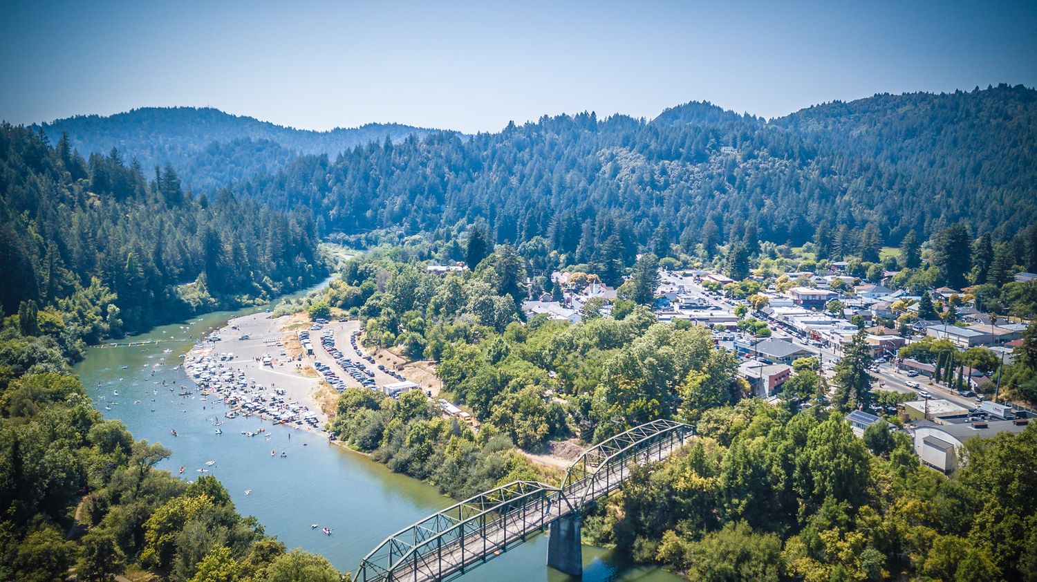 Scenic aerial view of a river bridge connecting a small town surrounded by forested mountains.