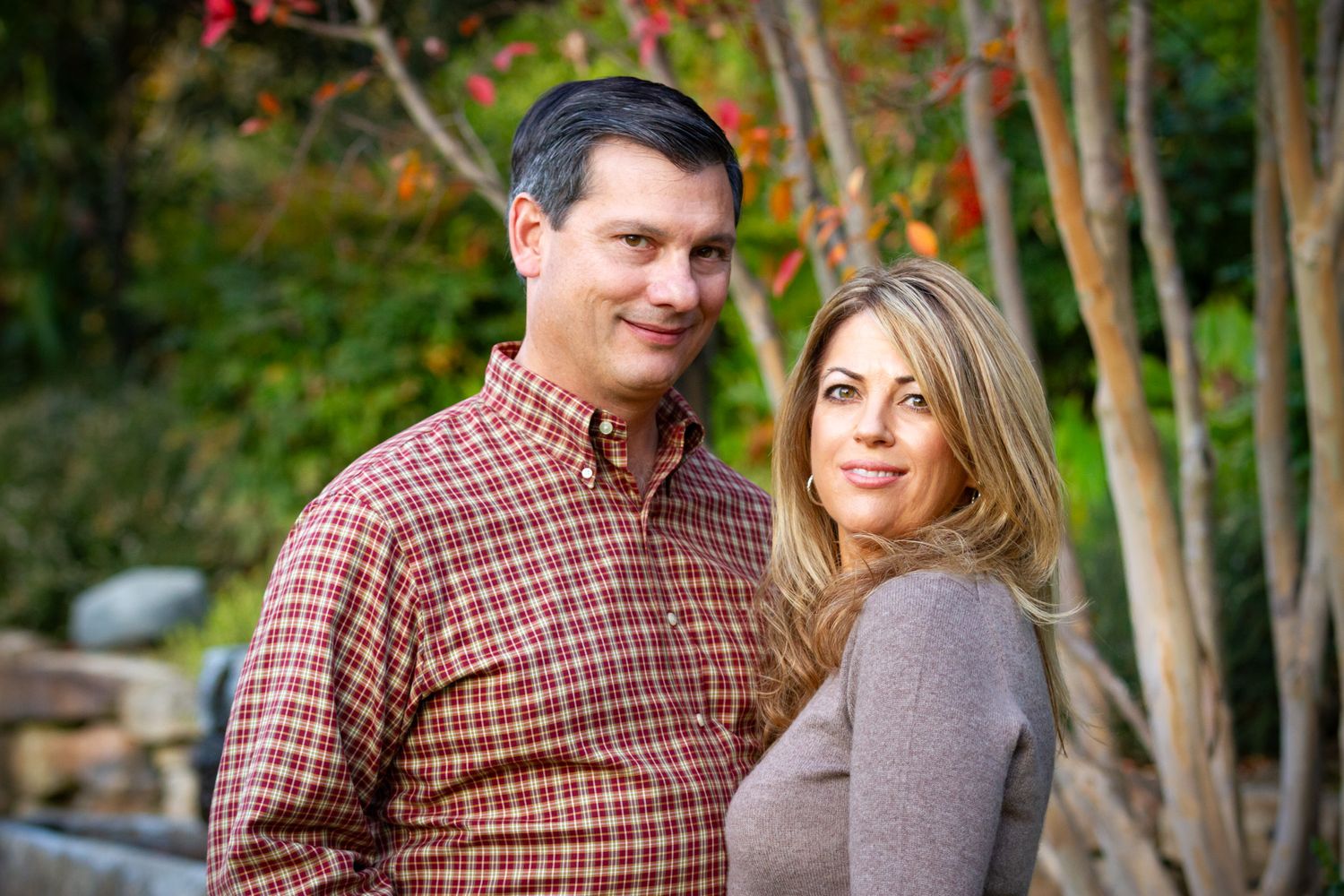 Romantic outdoor portrait of couple in coordinating casual outfits against autumn foliage.