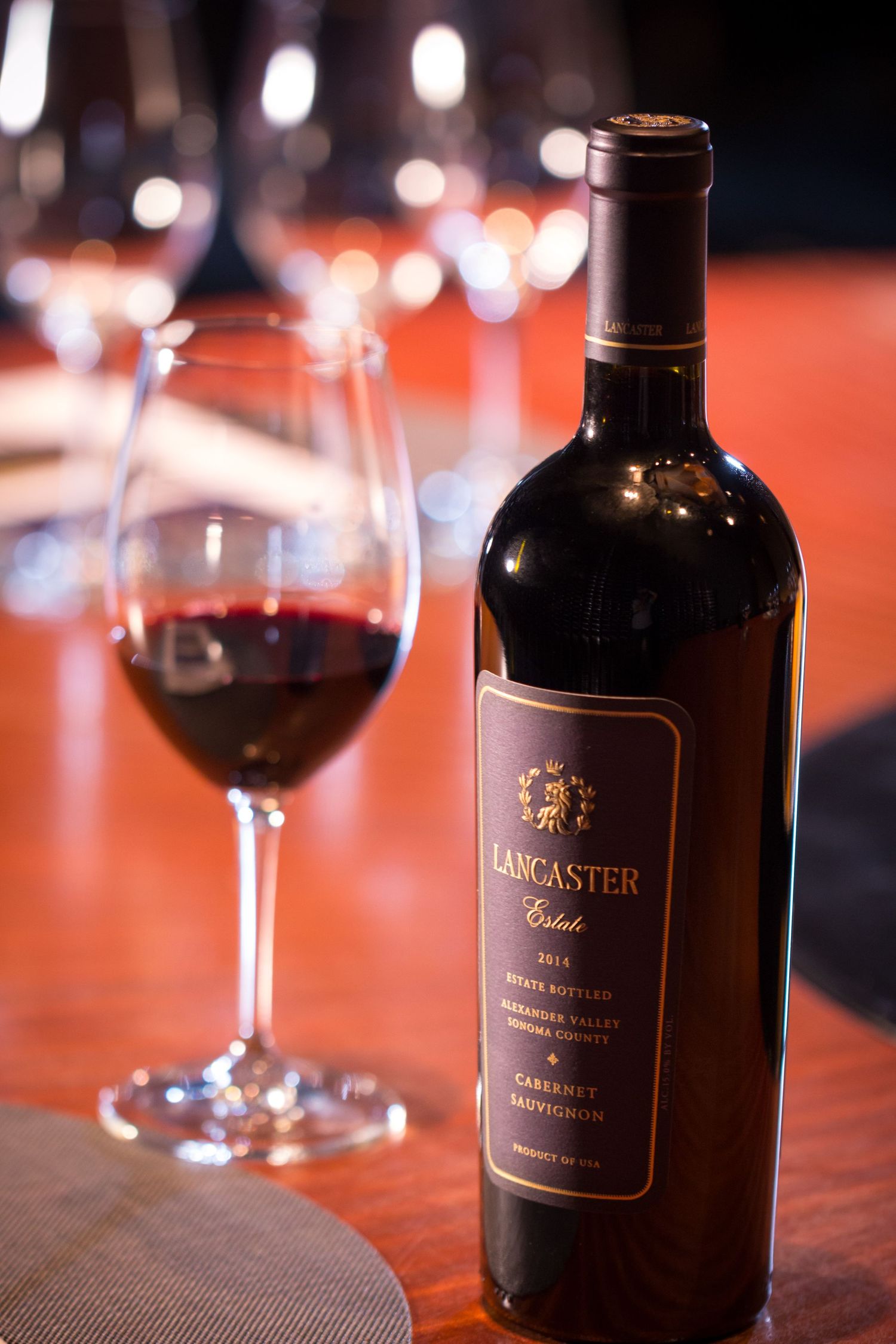 Lancaster Estate red wine bottle and glass on wooden table with ambient lighting.
