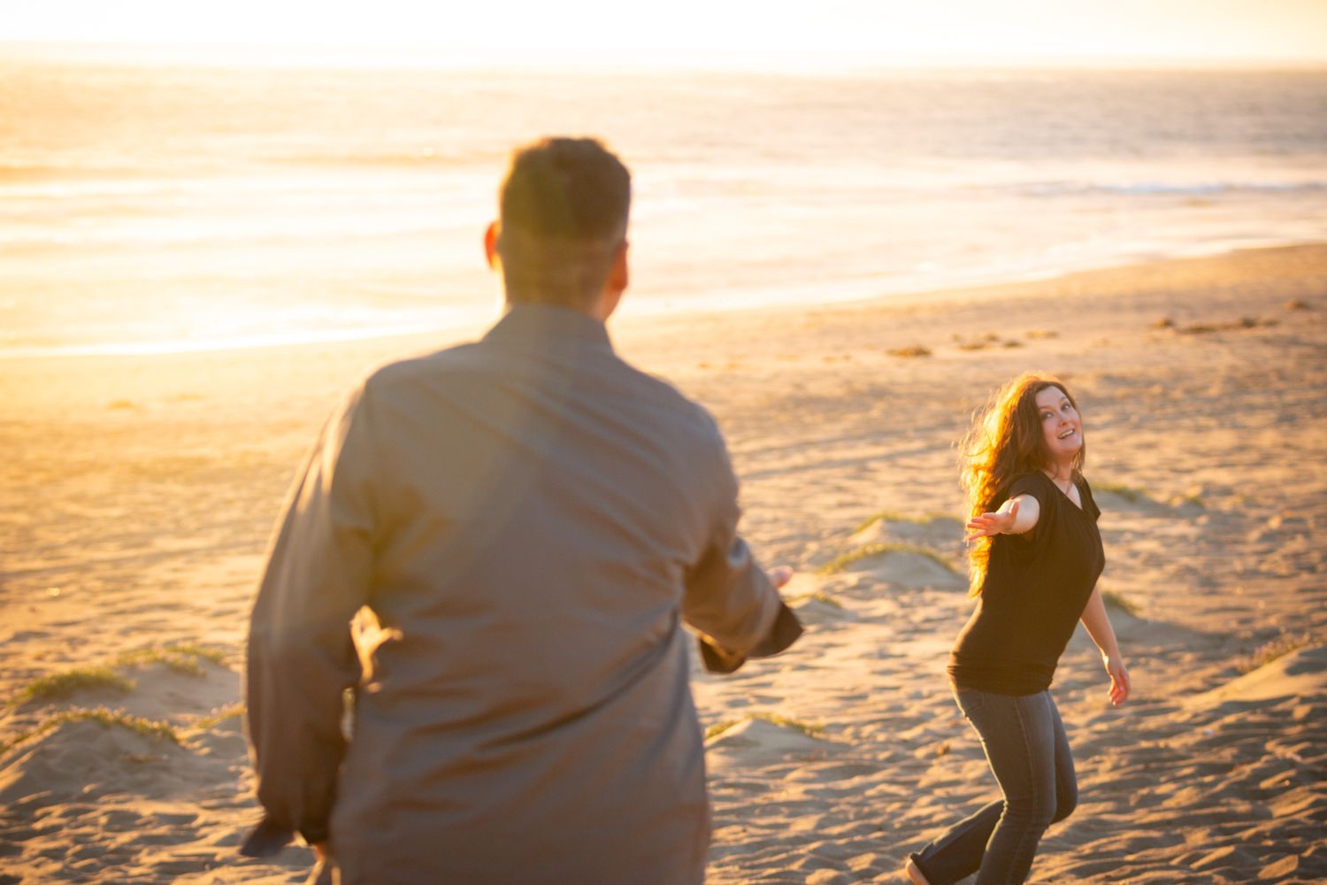 A playful couple enjoys a carefree moment on a sandy beach at sunset.