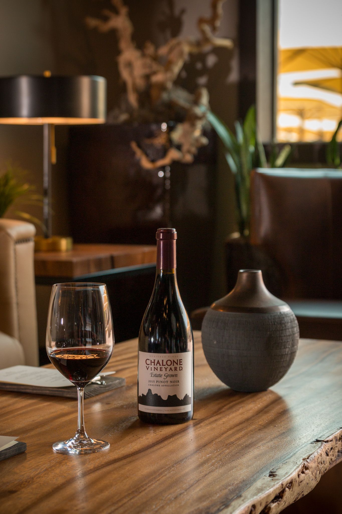 Chalone Vineyards wine bottle and glass displayed on live edge wood table with modern decor.