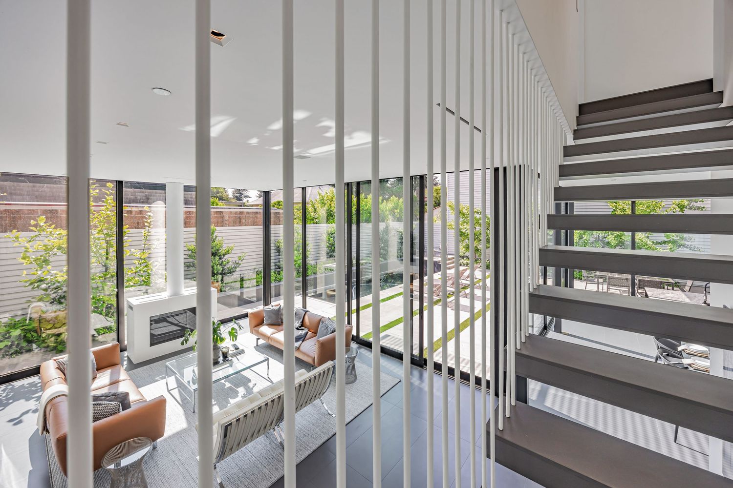 Contemporary staircase with vertical white railings overlooking an open-concept living space with glass walls.