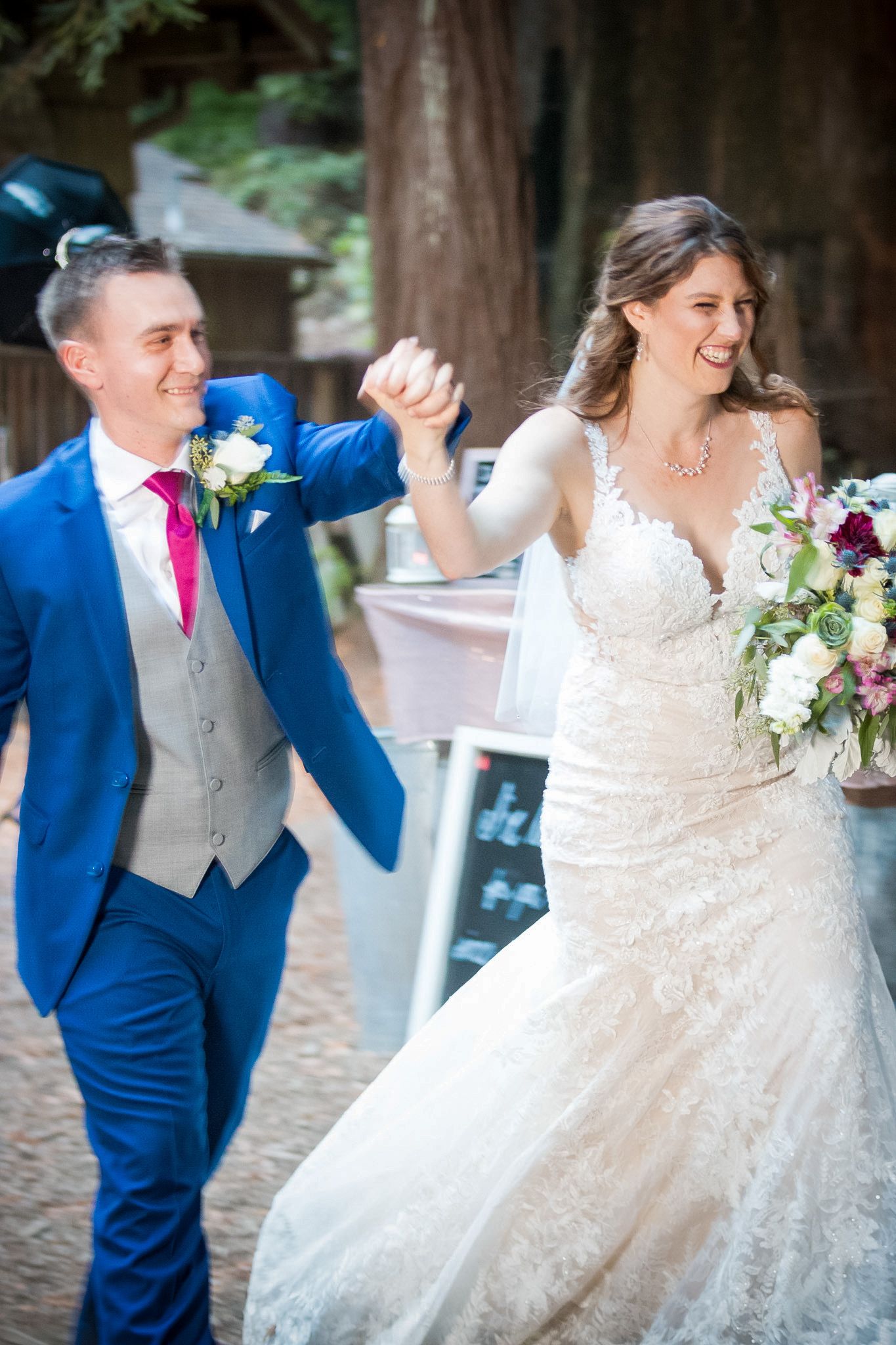 Celebratory moment of newlyweds dancing and holding hands at outdoor forest venue.