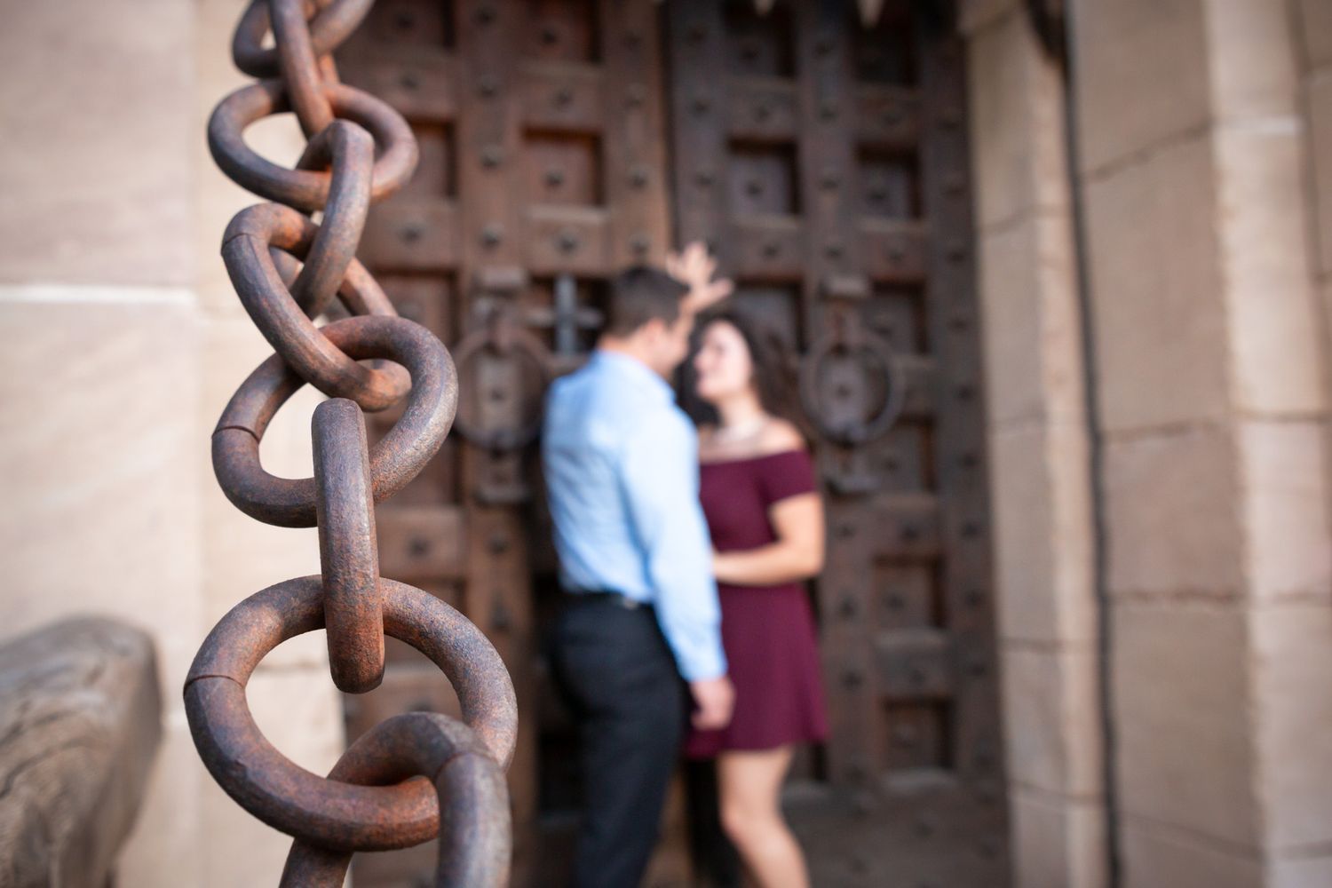 Rustic iron chains frame a couple against an ornate wooden castle door.
