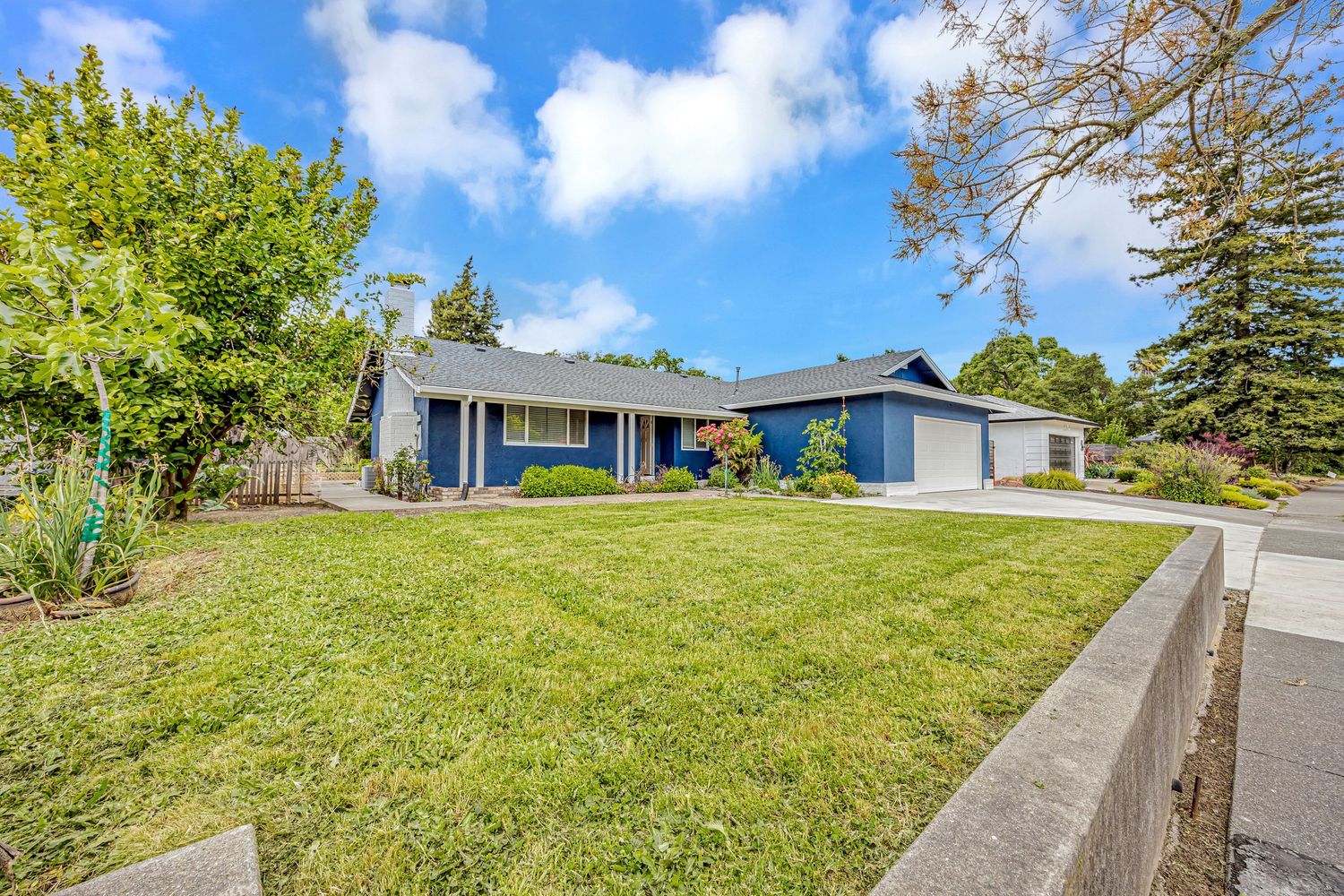 Blue ranch house with attached garage and green lawn under bright blue sky.