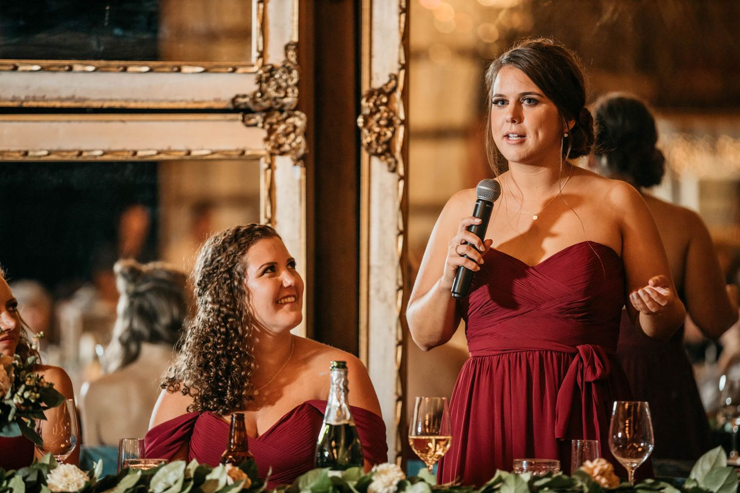 Bridesmaids in burgundy dresses give emotional wedding toasts at an elegant reception.